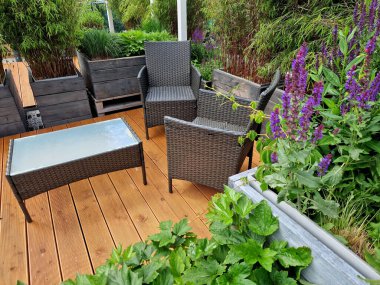 Teras ve rattan yapılmış hasır sandalyeler. Gayri resmi çiçek saksıları gri kalaslarla kaplı bir terasta ahşap bir bahçe.