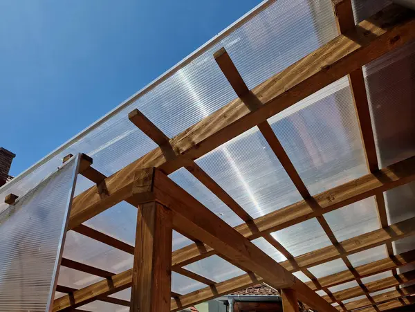 Ahşap pergola ve pleksiglass çatılı teras. Sarmaşıklar geriliyor, kirişlerin altında sürünüyorlar. Bahçe ya da park. Alkolsüz duvar şarabı bölgesinde oturuyor. Kırsal restoran Fransa, kiriş, küre, lamba