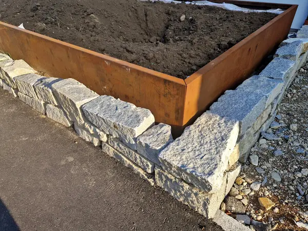 Çeşitli yükseklik ve şekillerdeki metal kaplar kaldırımı tuğla bina cephesinden işlek yoldan ayırıyor. Çalılar, çakıllar, mozaikler ve katmanlı saksılarda çalılarla daimi ve süslü otlar.