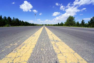 Otoyol, asfalt yol mavi gökyüzünün ve beyaz bulutların altında.
