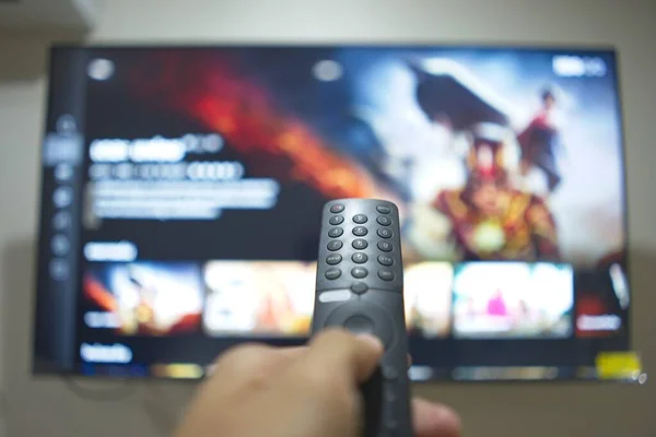 Hand with TV remote control, switching TV series from streaming service platform. The new way of enjoying entertainment at home.