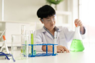 Çocuklar laboratuvarda biyoloji ve kimya öğreniyor. Bir STEM eğitim konsepti. BTMM sınıfında kimyasal deney şişesiyle çalışan Asyalı bir öğrenci..