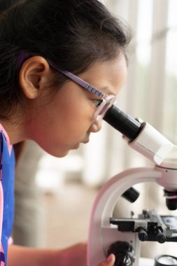 Çocuklar laboratuvarda biyoloji ve kimya öğreniyor. Bir STEM eğitim konsepti. BTMM sınıfında mikroskop kullanan Asyalı bir kız öğrenci..