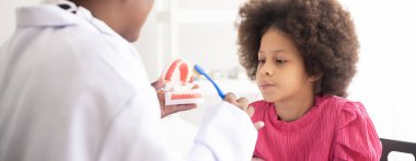 Afrikalı Amerikalı dişçi melez afro çocuğa diş fırçalamayı anlatıyor. Çocuklar için doktor ve sağlık konsepti.