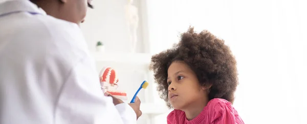 African American dentist explaining to mixed-race afro child how to brush teeth. The doctor and healthcare concept for children.