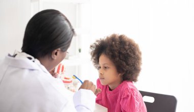 Afrikalı Amerikalı dişçi melez afro çocuğa diş fırçalamayı anlatıyor. Çocuklar için doktor ve sağlık konsepti.