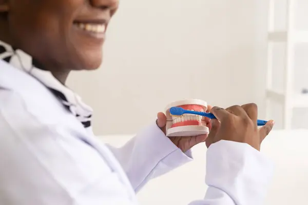 African American dentist. The dental care woman doctor showing up how to brush dental teeth model at the clinic to patient.
