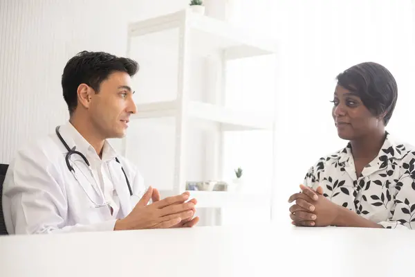 Hastanede steteskopu olan Afrikalı Amerikalı bir hastayı muayene eden İspanyol doktor. Sağlık hizmetleri tıbbi teşhisi ve incelemesi.
