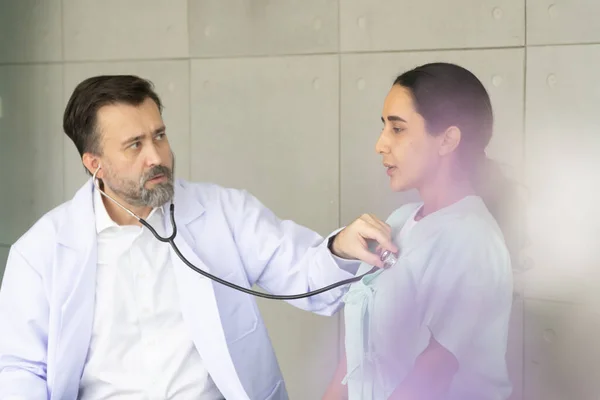 Caucasian male physician diagnosis for root cause finding by stethoscope with Hispanic female patient. The medical healthcare exam and check-up with the doctor concept.