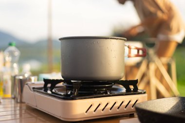 Kamp 'ta yemek aşığı! Doğal göl ve dağ manzaralı arka planda kamp yaparken yemek pişirmek. Eğlence ve seyahat, açık hava aktiviteleri yaşam tarzı..