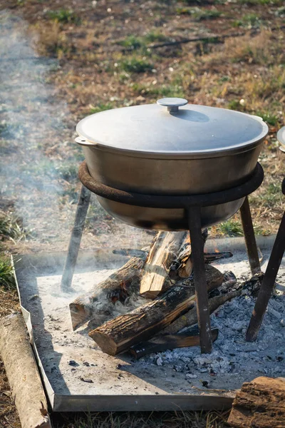 Kitchen outdoors, cooking at the stake, metal cauldron on the fire. Preparing of a food in black used cauldron on open fire, camping meal. Selective focus, shallow depth of field