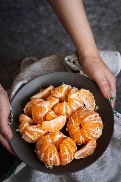 Tangerines in a bowl. The hands of a European woman hold a plate of peeled tangerines. Selective focus, dark and moody photo, shallow depth of field