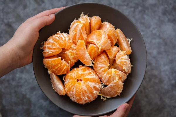 Tangerines in a bowl. The hands of a European woman hold a plate of peeled tangerines. Selective focus, dark and moody photo, shallow depth of field