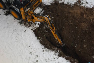 Tiraspol, Moldova - 31 Ocak 2023: JCB kazıcı bulutlu bir kış gününde kanalizasyon borusu döşemek için hendek kazıyor. Seçici odak, yüzeysel alan derinliği