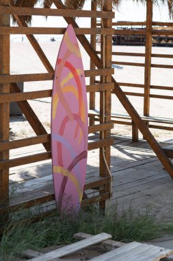 Renkli çizgili sörf tahtası. Romanya 'nın Köstence kentinde bir sahil tepe örtüsünün altında sörf tahtası.
