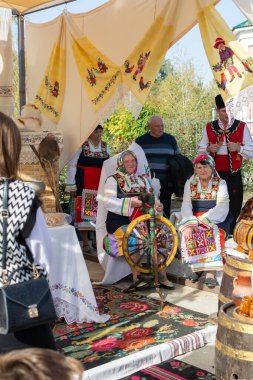 Bender, Moldova - 21 Ekim 2023: Bulgaristan 'ın ulusal kostümlü yaşlı erkek ve kadınları, eski nitelikleri, dönen halılar, havlular. Şarap Festivali 'nde halk sanatı sergisi
