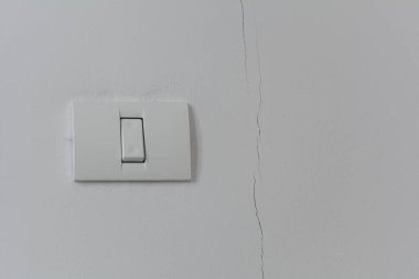 Beyaz bir duvarda beyaz plastik bir düğme. Düğmenin sağında duvarın yüksekliğinde bir çatlak var..