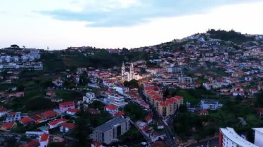 Portekiz, Madeira, Funchal 'daki tarihi bir kiliseyi çevreleyen hava aracı görüntüleri. Klipte, şehrin büyüleyici kentsel manzarasıyla çevrili kırmızı kiremitli çatıları olan geleneksel Portekiz mimarisi sergileniyor.. 