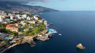Portekiz 'in Madeira, Funchal kıyı şehrinin insansız hava aracı görüntüleri. Video klipte Atlantik Okyanusu yakınlarındaki geleneksel kırmızı çatılı binalar, dolambaçlı sokaklar ve manzaralı dağ manzaraları yer alıyor.. 