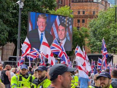 Manchester, İngiltere, 2 Ağustos 2025. İngiltere 'nin kentteki ilk protesto yürüyüşü şehir merkezinde sendika bayrakları ve sağcı protestocuları gösterirken, polis ekranda Donald Trump' ın görüntüsü ve görüntüsü yer alıyor.