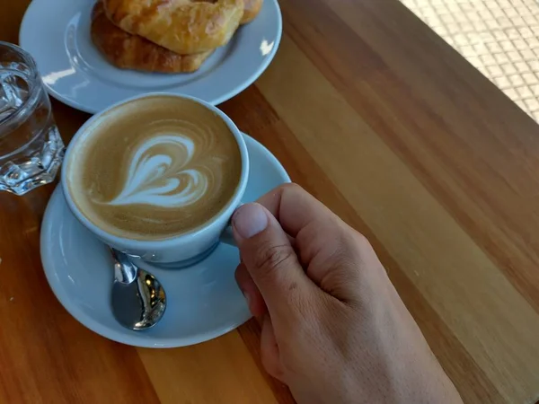 cup of coffee with a heart-shaped drawing hand holding a latte about to have breakfast