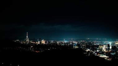 Geceleri gökyüzünde bulutlar hareket ediyor. Neon ışıkları canlı şehir manzarasında parlıyor. Dağlarla çevrili şehrin gece manzarası sisli ve rüya gibi Taipei City, Tayvan