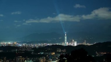 Kulenin tepesindeki mavi lazerlerden gelen ışık her yöne doğru parlıyor. Dağlarla çevrili şehrin gece manzarası sisli ve rüya gibi Taipei City, Tayvan