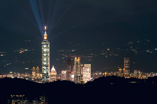 Kulenin tepesindeki mavi lazerlerden gelen ışık her yöne doğru parlıyor. Dağlarla çevrili şehrin gece manzarası sisli ve rüya gibi Taipei City, Tayvan