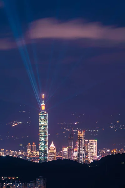 The light from the blue lasers on top of the tower shines in all directions. Night view of the city surrounded by mountains is hazy and dreamy.. Taipei City, Taiwan