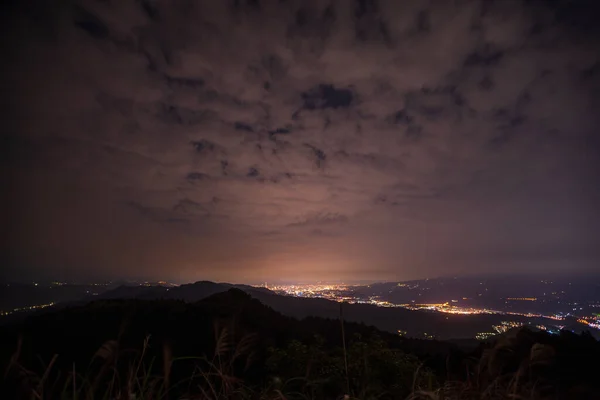 Clouds moving in the sky at night. Neon lights shine on the vibrant cityscape. Ruifang Wufen Mountain, New Taipei City, Taiwan