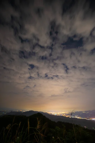 Clouds moving in the sky at night. Neon lights shine on the vibrant cityscape. Ruifang Wufen Mountain, New Taipei City, Taiwan