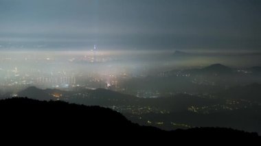 Clouds moving in the sky at night. Neon lights shine on the vibrant cityscape. Hazy and dreamy city night view. Lion's Head Mountain, New Taipei City, Taiwan