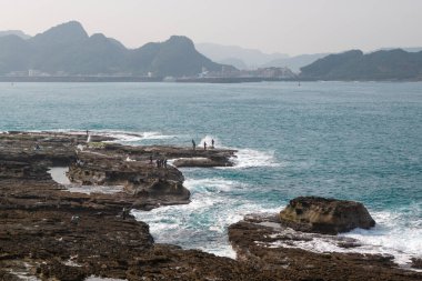 White waves lap against the rocks. Some people stood on the rocks and fished. Ruifang Rocky Beach, New Taipei City, Taiwan.