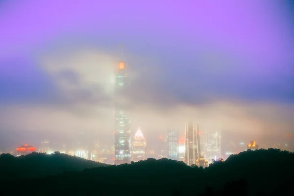 Clouds moving in the sky at night. Neon lights shine on the vibrant cityscape. Night view of the city surrounded by mountains is hazy and dreamy. Taipei City, Taiwan