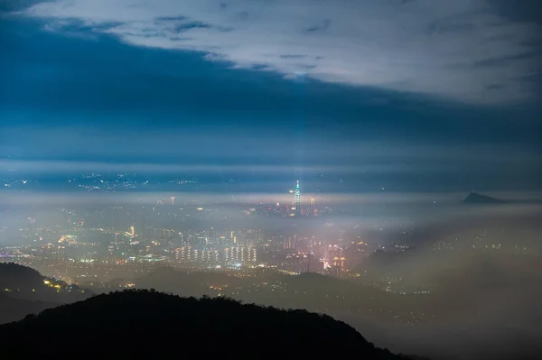 Clouds moving in the sky at night. Neon lights shine on the vibrant cityscape. Hazy and dreamy city night view. Lion\'s Head Mountain, New Taipei City, Taiwan