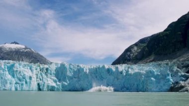 Muhteşem bir buzul yavrusu. Buz küpleri bir patlama gibi suya düştü. Mavi bir nehre dökülen kayıktan görünen buzdan bir duvar. Alaska 'da yaz.