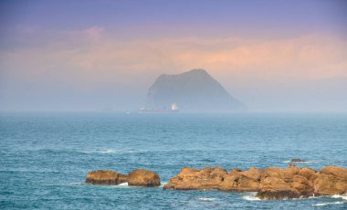 Sis içinde küçük bir ada. Yük gemisi denizde yelken açıyor. New Taipei 'deki Wanli Sahili' nden Keelung Adası manzarası. Tayvan.