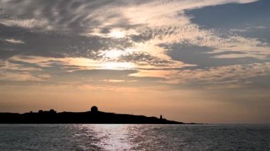 Gün batımında, güneş ufka doğru gider, deniz fenerinin silueti. Fugui Burnu Deniz Feneri, günbatımı çekimleri ve turistik yerleriyle ünlüdür..
