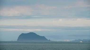 Tekne adanın etrafında döner. Biraz sis ve renkli bulutlar var. New Taipei 'deki Wanli Sahili' nden Keelung Adası manzarası. Tayvan.