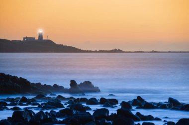 Güneş alacakaranlıkta fenerin arkasında. Shimen 'deki Fugui Burnu Deniz Feneri. Tayvan