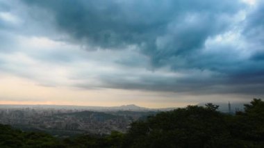 Kara bulutlar hızla hareket ediyor. Turuncu gün batımı. Alacakaranlıkta, bulutlu bir günde Taipei şehrinin manzarası.