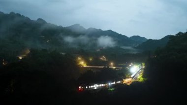 Sarı bir dizel tren istasyona giriyor. Bulutlu dağlar ve ormanlar. Pingxi hattı boyunca nehir vadileri, çukurlar ve şelaleler var. Tayvan