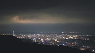 Gökyüzünde dinamik bulutlar olan parlak ışıklı Taipei şehri gece sahnesi. Wufenshan Hava Radar İstasyonu dağın tepesinde duruyor. Tayvan