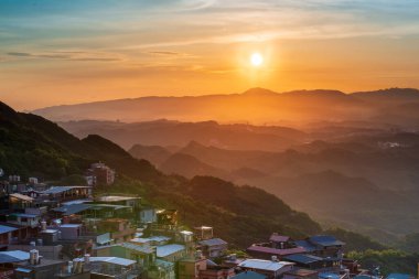Göz kamaştırıcı alacakaranlık manzarası - canlı turuncu gökyüzü, dinamik bulutlar, sisli dağlar. Tayvan 'ın Jiufen kıyı köyünü çevreleyen Serene Okyanusu.