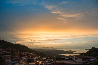 Göz kamaştırıcı alacakaranlık manzarası - canlı turuncu gökyüzü, dinamik bulutlar, sisli dağlar. Tayvan 'ın Jiufen kıyı köyünü çevreleyen Serene Okyanusu.