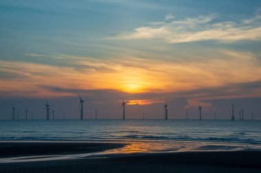 Rüzgâr türbinlerinin hayranları köpüklü denizin üzerinde dönüyorlar. Gün batımında dinamik bulutlar. Tayvan 'ın kuzeybatı kıyısında bir rüzgar çiftliği. Yeşil güçten biri.