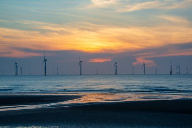 Rüzgâr türbinlerinin hayranları köpüklü denizin üzerinde dönüyorlar. Gün batımında dinamik bulutlar. Tayvan 'ın kuzeybatı kıyısında bir rüzgar çiftliği. Yeşil güçten biri.