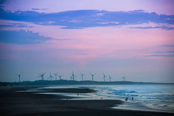 Fans of wind turbines spin over the sparkling sea. Dynamic clouds at sunset. An offshore wind farm off the northwest coast of Taiwan. One of green power.