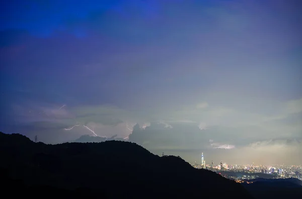 Dreamy cityscape shrouded in clouds. Lightning flashes in the sky. Night view of the city surrounded by mountains is hazy and dreamy. Dajianshan, Taiwan