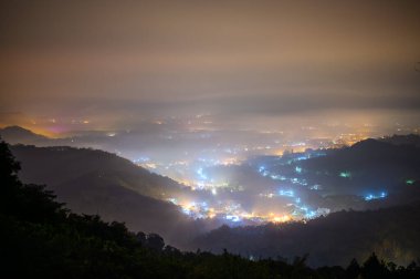 Bulutlarla çevrili bir vadideki aydınlanmış köylerin renkli bir gece görüntüsü. Nantou ilçesindeki Yuchi kasabasındaki Jinlong Dağı 'nın gece manzarası. Tayvan